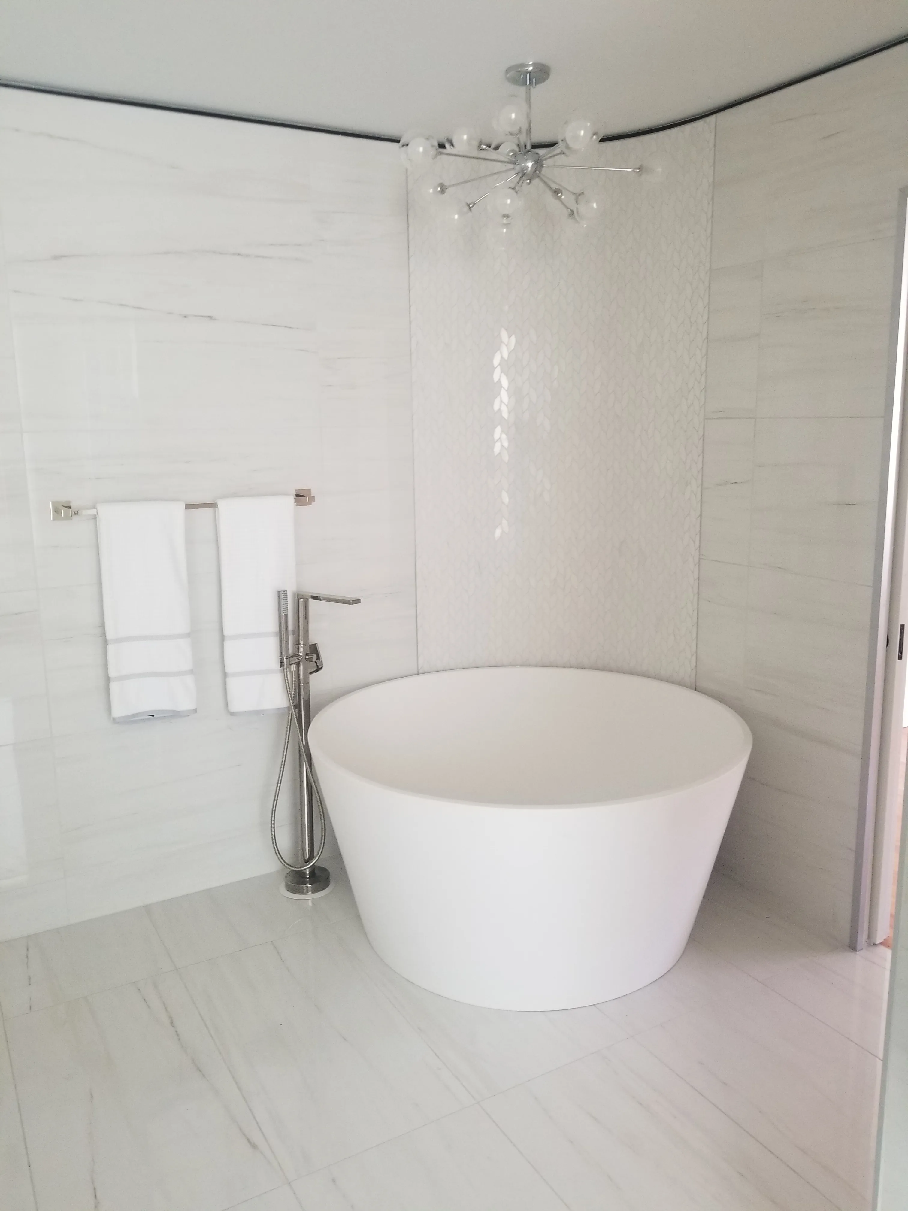 Freestanding soaking tub placed inside a tiled shower area with white wall tiles and handheld fixture