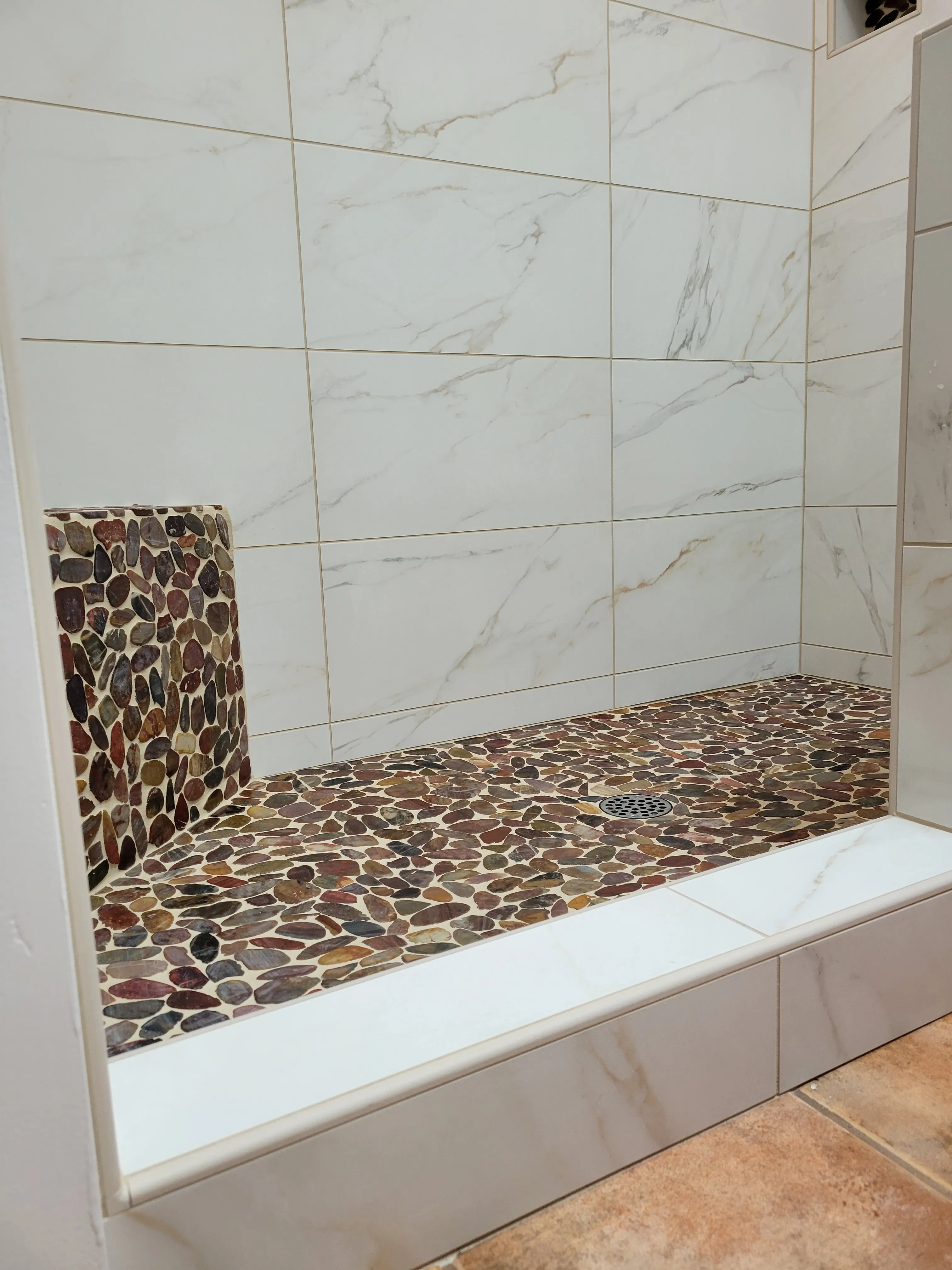 Pebble mosaic shower bench and curb detail with marble-look wall tiles