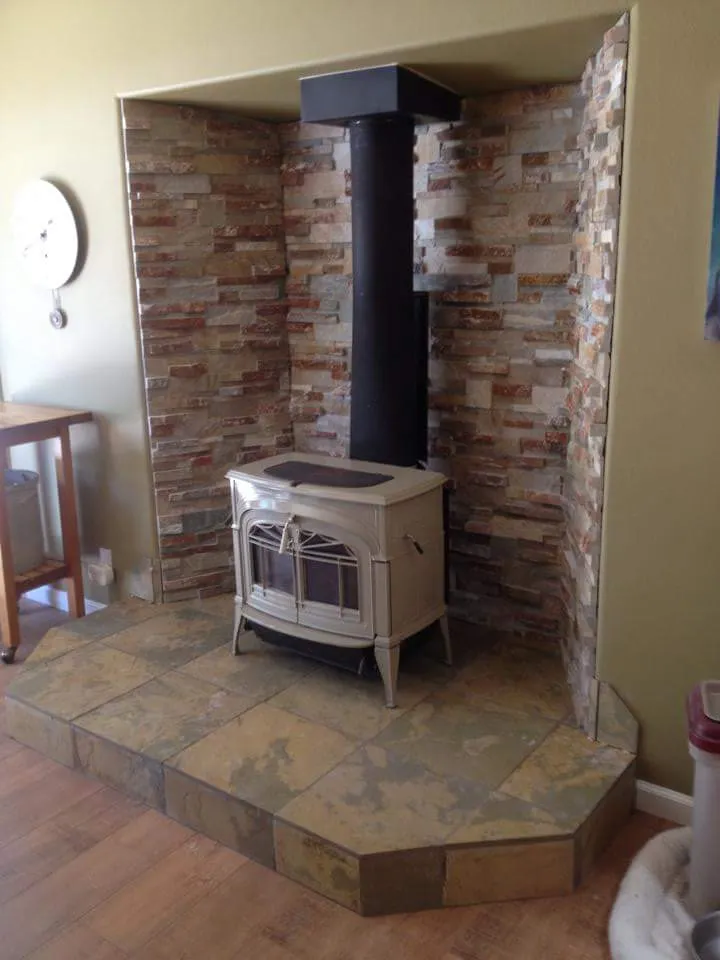 Stacked stone fireplace alcove with freestanding wood stove and raised hearth